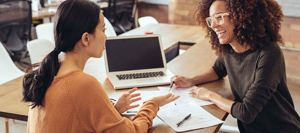 two women discussing paperwork at a desk