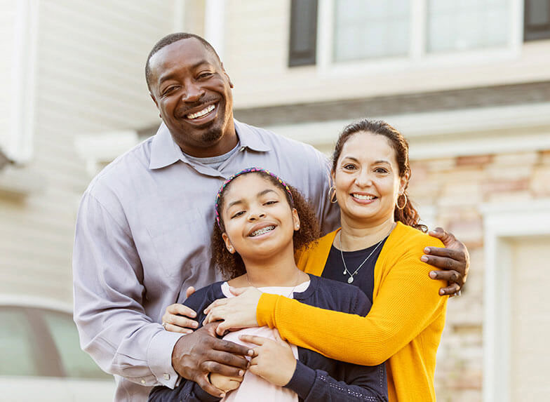 Family smiling and hugging outside of their new home